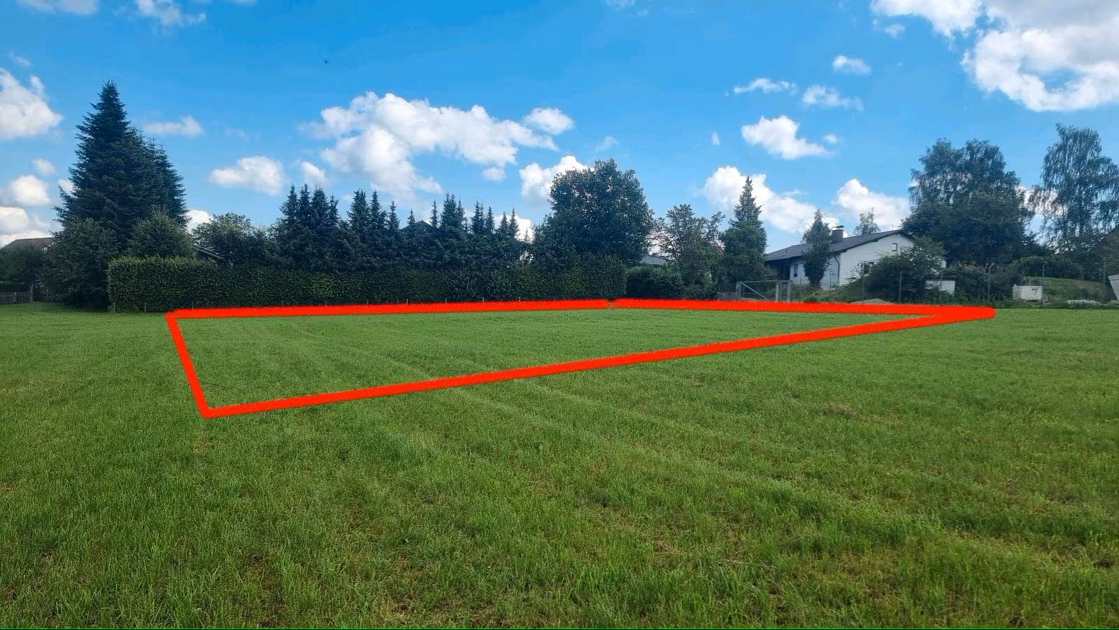 Wiese bei Painten im Naturpark Altmühltal mit rot markiertem Tiny House Bauplatz vor Häusern und Bäumen