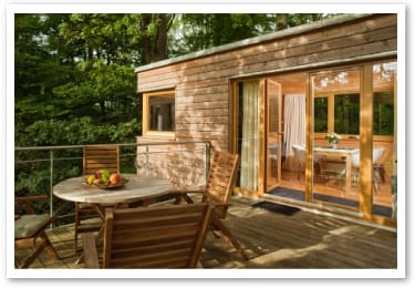 Terrasse einer Baumhaussuite im Resort Baumgeflüster mit Holztisch, zwei Stühlen und Obstschüssel