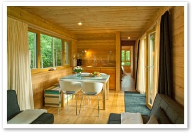 Innenansicht eines Baumhauses im „Resort Baumgeflüster“ mit Holzwänden, Esstisch und einem dahinterliegenden Raum