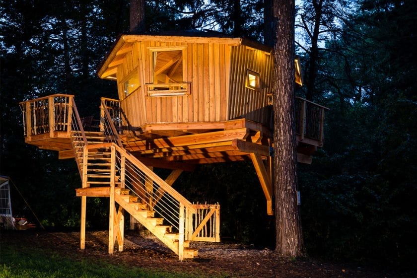 Baumhaus Cuxhaven bei Nacht, das Haus ist aus Holz mit Treppe und Geländer, im Wald zwischen Bäumen