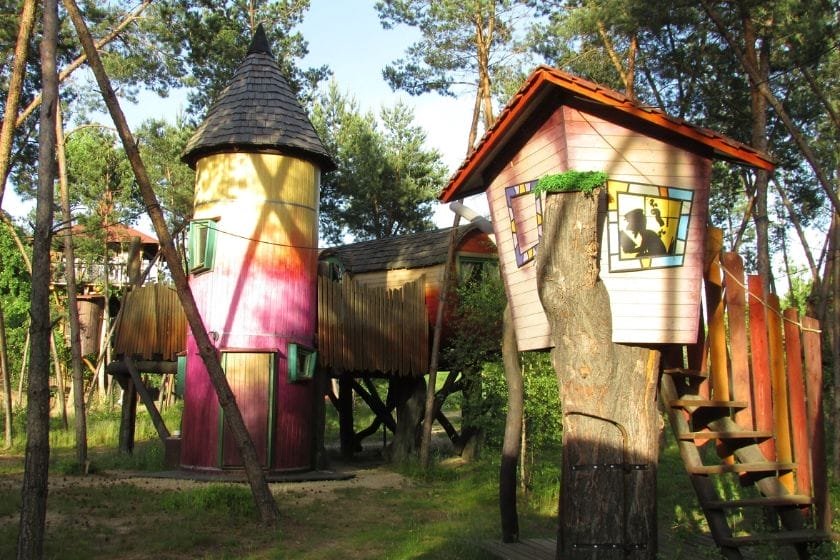 Bunte Baumhäuser und Holzhütten in der Kulturinsel Einsiedel, umgeben von Bäumen und grüner Vegetation
