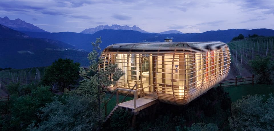 Ein modernes Modulhaus aus Holz und Glas auf einem Hügel mit Weinreben und Bergpanorama in den Bergen