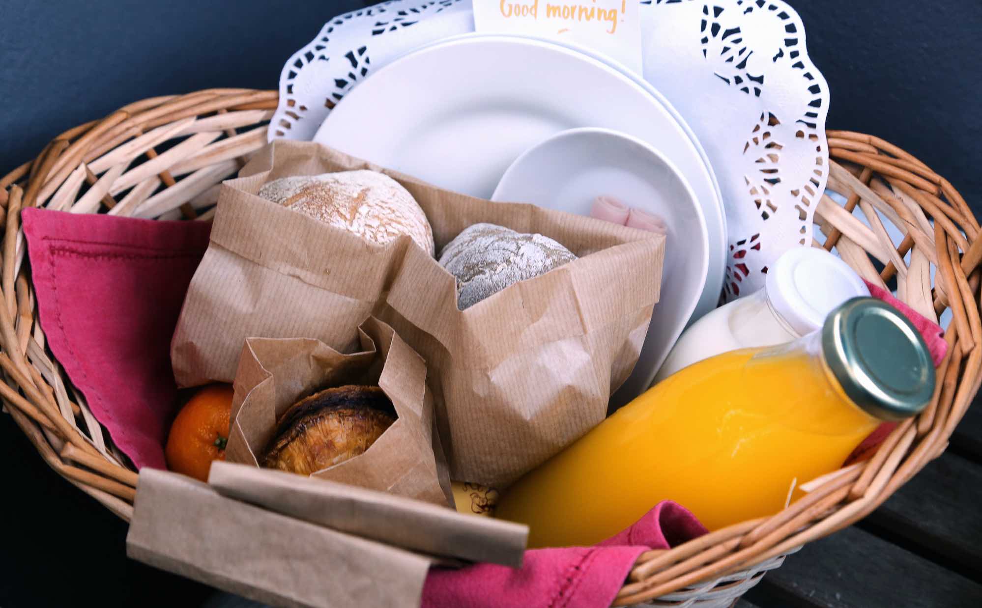Ein Willkommenskorb mit Brötchen, Orangensaft, Milch, Geschirr und einer Mandarine