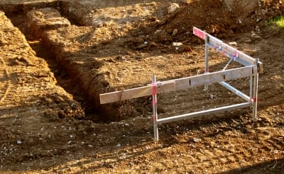 Ausgehobener Fundamentgraben auf einer Baustelle mit Messlatte für die Ausrichtung