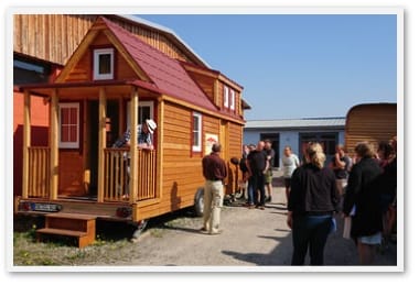 Mehrere Menschen begutachten ein Tiny House auf Rädern, das vor einem Gebäude steht
