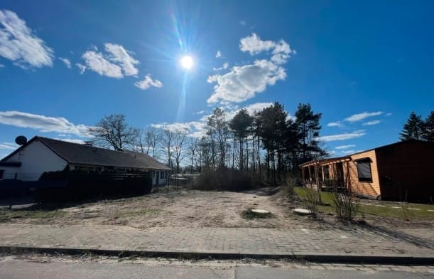 Sonnenbeschienenes Pachtgrundstück in Suderburg mit angrenzenden Häusern, Waldrand und blauem Himmel
