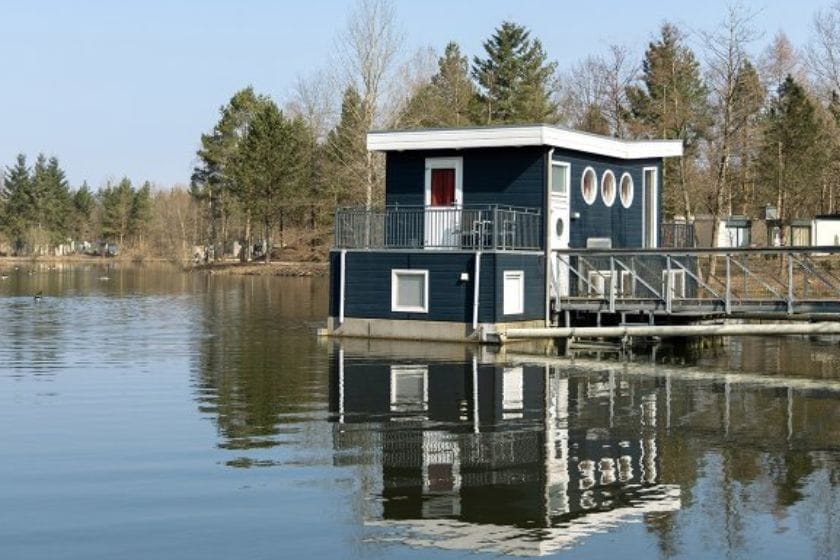 Ein dunkelblaues Hausboot mit roter Tür und Balkon, am Steg eines Sees im Center Parc Bispinger Heide