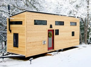 hOMe Tiny House mit Holzfassade und roter Eingangstür im Schnee