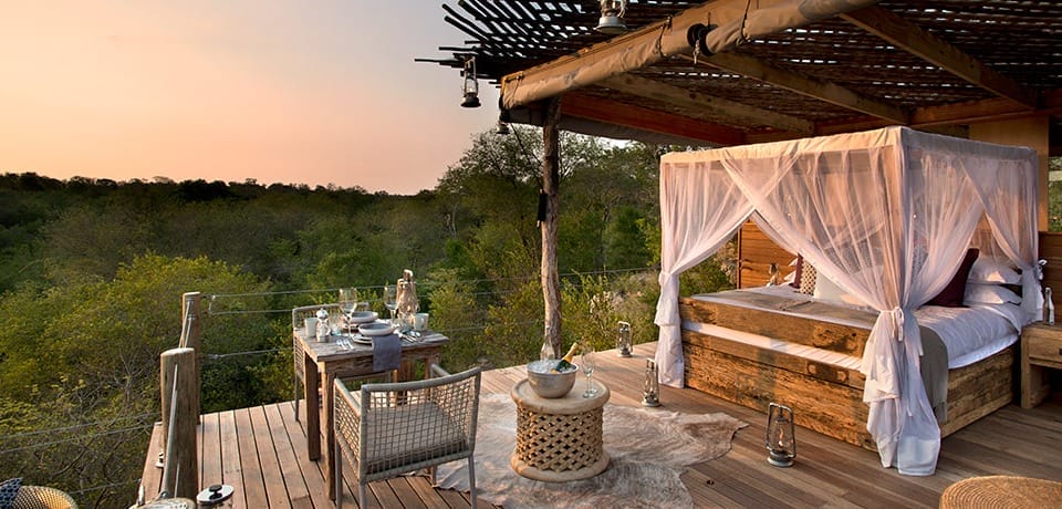 Romantisches Baumhaus-Schlafzimmer mit Himmelbett, Essbereich und Blick auf einen Wald bei Sonnenuntergang