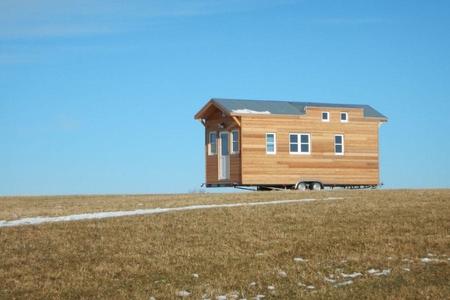 Tiny House vom Hersteller Kleiner Nomade auf einem Anhänger stehend, umgeben von trockenem Gras unter blauem Himmel