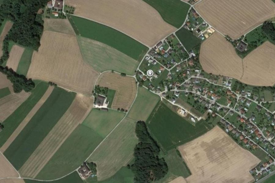 Satellitenansicht der Ortschaft Neuhofen mit Ackerflächen, Waldstücken und Bebauung, einem roten Pin markierten Grundstück is