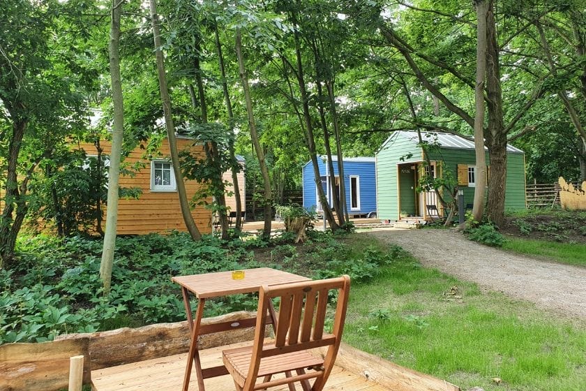 Drei Tiny Houses in Gelb, Blau und Grün stehen im Wald auf dem Gelände des Pier 9 Tiny-House-Hotels in Hamm