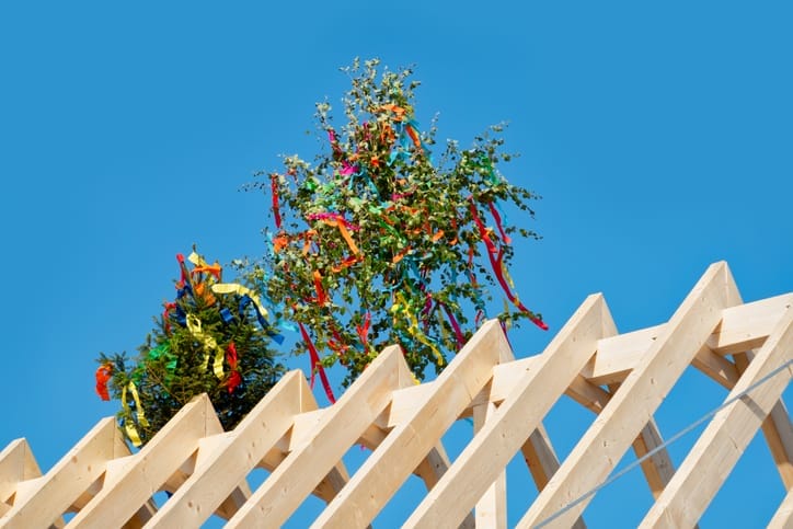 Dachstuhl eines Rohbaus mit Richtbaum und bunten Bändern vor blauem Himmel