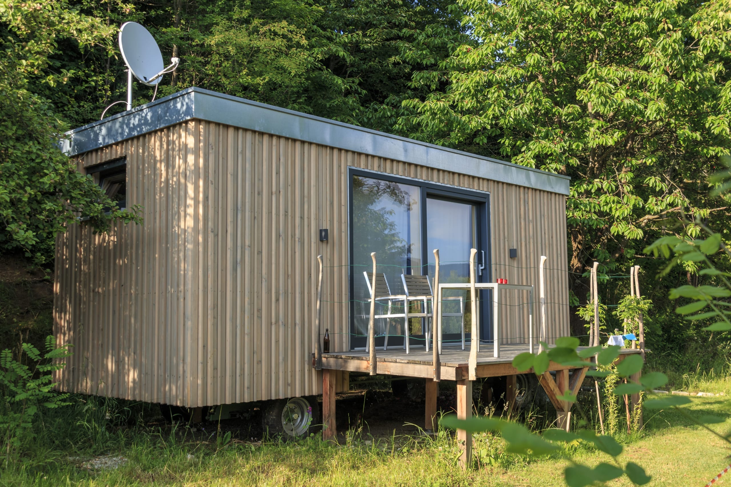 Gesamtansicht des Tiny House „Steirermadl“ mit begrünter Umgebung, Terrasse und Satellitenschüssel