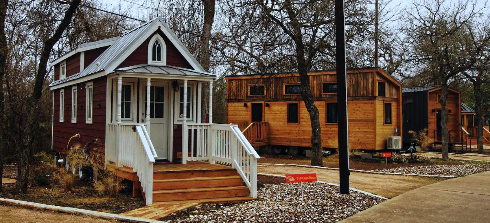 Mehrere Tiny Houses in einem Park, vorne ein rotes Haus mit weißer Veranda, dahinter Holzhäuser